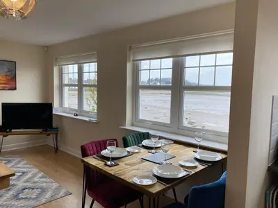 a dining room with a table with chairs and windows at Harbourside in Garlieston