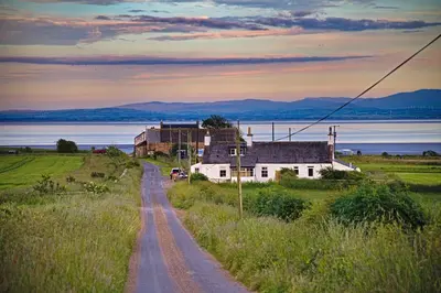 a house on the side of a road next to the water at Arthur's Cottage in Dumfries