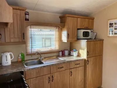 a kitchen with wooden cabinets and a sink and a microwave at Happy Days Holiday Home Whithorn2 in Newton Stewart