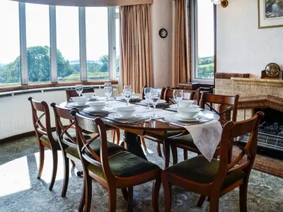 a dining room with a table and chairs and windows at Woodend Farmhouse Halmyre in Haugh of Urr