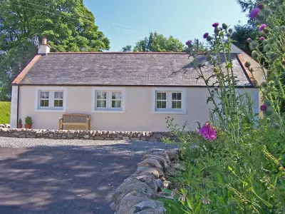 a white house with a bench in front of it at Arden Cottage in Twynholm