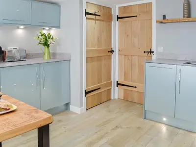 a kitchen with white cabinets and wooden floors at The Old Toll House in Portpatrick
