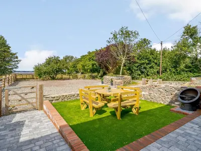 a wooden table and chairs in a yard with a fence at The Barnacle Goose - Uk35261 in Bowness-on-Solway
