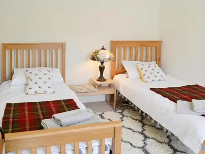 a bedroom with two beds and a table with a lamp at Oor Wee Hoose in Whithorn