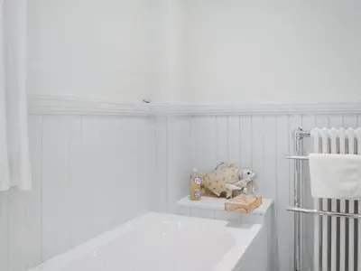 a white bathroom with a tub and a towel rack at Field Cottage in Old Bridge of Urr