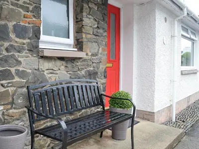 a black bench in front of a house with a red door at Thistle Cottage in Portpatrick