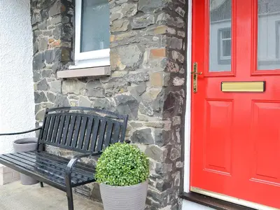 a bench next to a red door with a plant at Thistle Cottage in Portpatrick