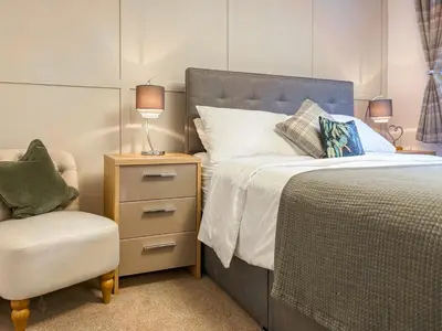 a bedroom with a bed and a chair and a lamp at Thistle Cottage in Portpatrick