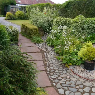 a garden with a stone path with flowers and bushes at Belmont Cottage in Dumfries