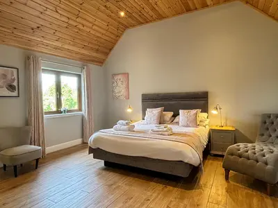 a bedroom with a bed and a chair and a window at Osprey Lodge 8 with Hot Tub in Newton Stewart