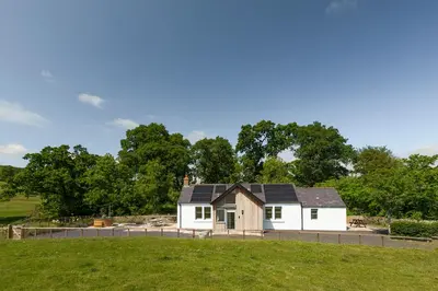 a white house with black roof in a field at Slatehouse Cottage, Drumlanrig in Thornhill