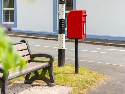a bench and a red mailbox next to a street at Highgate in Kirklinton
