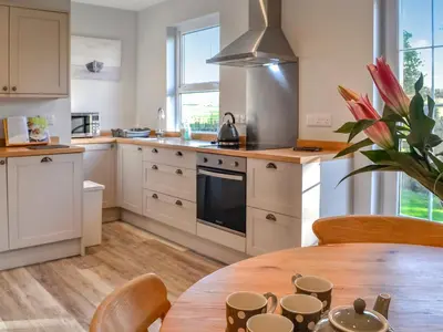a kitchen with white cabinets and a wooden table at Clarksburn Blue in Monreith
