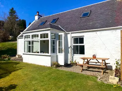 a white cottage with a picnic table in the yard at Wee Silverburn in Whiting Bay