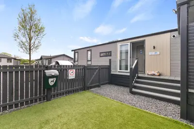 a house with a fence and a yard at Arranview Lochside Pods & Lodges all with private Hot-tubs in Fenwick