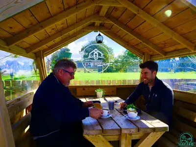 two men sitting at a wooden table in a shed at Arranview Lochside Pods & Lodges all with private Hot-tubs in Fenwick