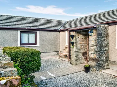 a house with a stone wall and a chair at Scalelands Cottage in Frizington