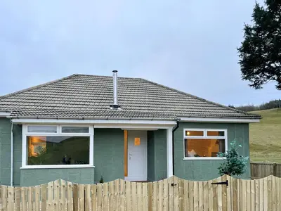 a green house with a wooden fence in front of it at Mossdale Cottage in Dalmellington