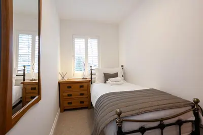 a white bedroom with a bed and a mirror at Keswick Ground floor apartment with parking in Keswick