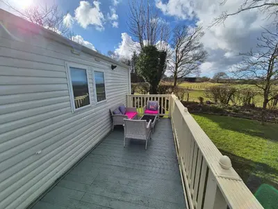 a deck with chairs and tables on a house at 24 The Beeches Caravan Park in Gilcrux
