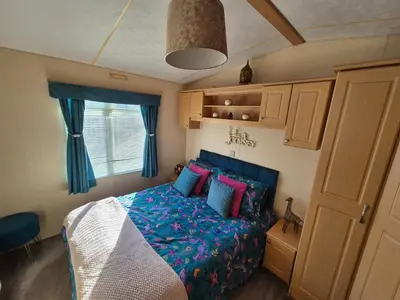 a bedroom with a bed with blue and pink pillows at 24 The Beeches Caravan Park in Gilcrux