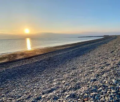 a beach with the sun setting over the water at The Rabbit Hill Holiday Home in Ballantrae
