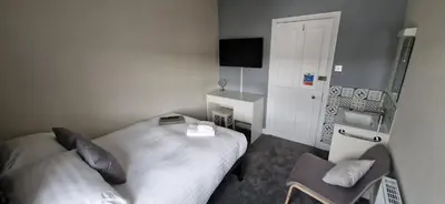 a small bedroom with two beds and a chair at Glencoe Guest House in Keswick
