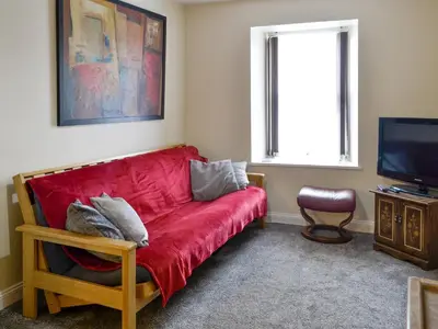 a living room with a red couch and a television at Brae Cottage in Whithorn