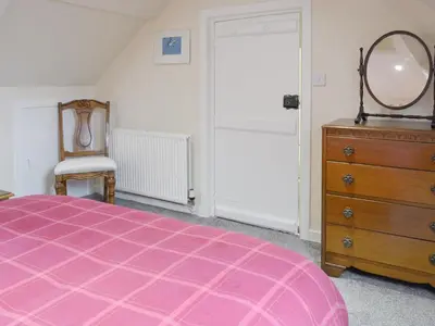 a bedroom with a pink bed and a dresser and a mirror at Brae Cottage in Whithorn