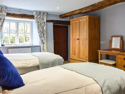 a bedroom with two beds and a wooden cabinet at Forge Cottage in Keswick