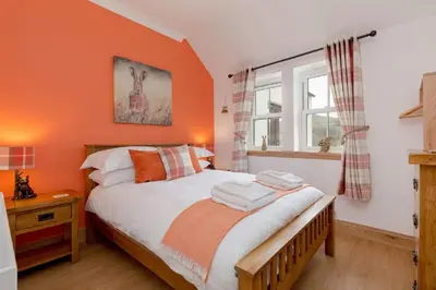 a bedroom with orange walls and a bed and a window at Balbeg Cottage in Straiton