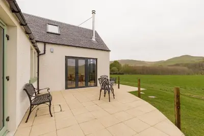 a patio with chairs and a house with a field at Balbeg Cottage in Straiton
