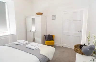 a white bedroom with a bed and a yellow chair at The Mila - Ayr Racecourse - Coorie Doon Stays in Ayr
