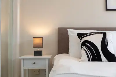 a bed with a black and white pillow and a lamp at London Gate No1 - Donnini Apartments in Kilmarnock