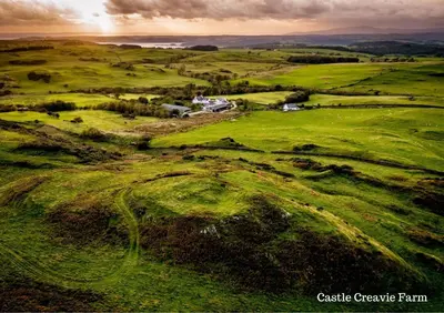 an aerial view of a green field with a house at The Steading at Castle Creavie Farm in Kirkcudbright
