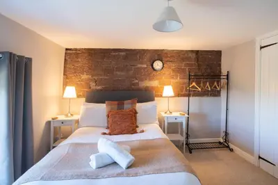 a bedroom with a large bed with two tables and a clock at Gatesgarth Cottage @ The Pheasant Inn in Brampton