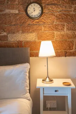 a bedroom with a bed and a clock on a brick wall at Gatesgarth Cottage @ The Pheasant Inn in Brampton