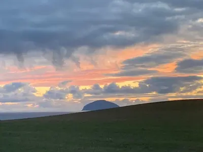 a sunset over a field with a mountain in the distance at Carnoustie 24 - Turnberry Holiday Park - short walk to beach in Girvan