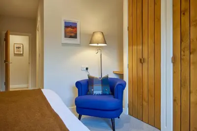 a bedroom with a blue chair and a lamp at Howe Keld 5 First Floor in Keswick