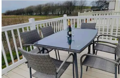 a table with chairs and a bottle of wine on a deck at AJL Caravan Rentals in Turnberry