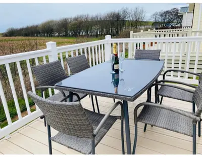 a table with chairs and a bottle of wine on a deck at AJL Caravan Rentals in Turnberry
