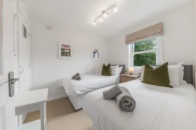 a white bedroom with two beds and a window at Derwent Cottage in Keswick