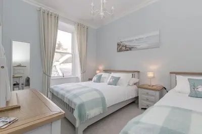 a white bedroom with two beds and a window at Carlton House Portpatrick in Portpatrick