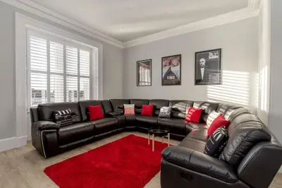a living room with a black leather couch and a red rug at Carlton House Portpatrick in Portpatrick
