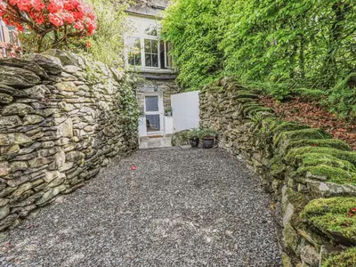 a stone wall next to a house with a door at Wisteria in Ambleside