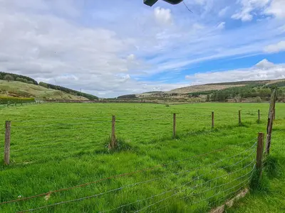 a fence in a field next to a field of grass at Craik Forestry Cottage in Teviothead