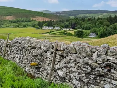 a stone wall with a field and houses in the background at Craik Forestry Cottage in Teviothead