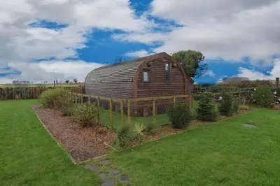 a large wooden barn in a field of grass at The Galloway Steading- The Bee Hive Couples Retreat with Hot Tub and Fire Pit in Glenluce
