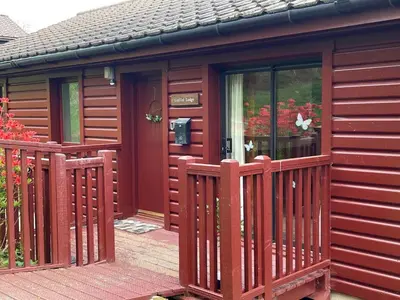 a red cabin with a wooden fence and flowers at Beautiful 3BR Lodge - Stunning Beach and Golf Location - Pass the Keys in Dalbeattie