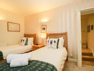 a bedroom with two beds and a stairway at Raphael's Cottage in Keswick